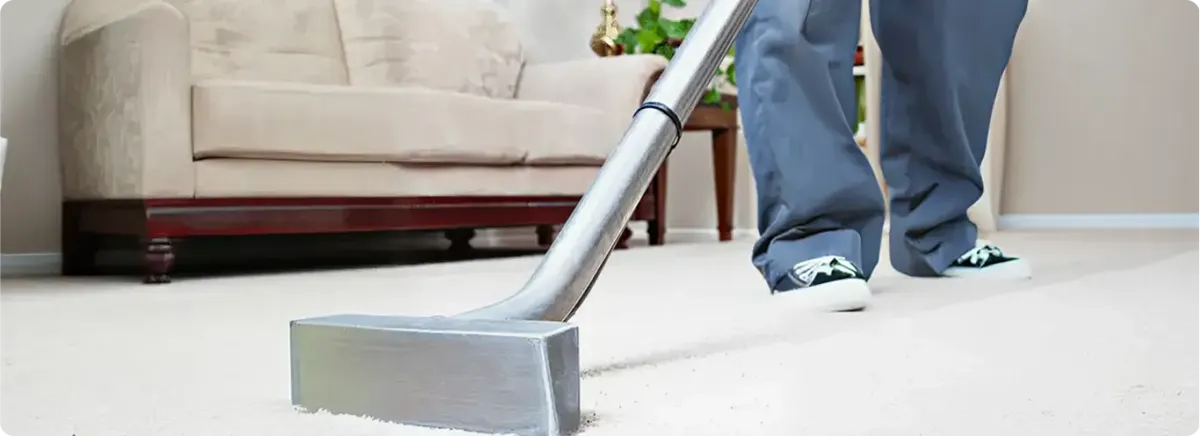 Carpet cleaning technician using a hot-water extraction wand on a light-colored carpet in a living room, Jackson, MS.